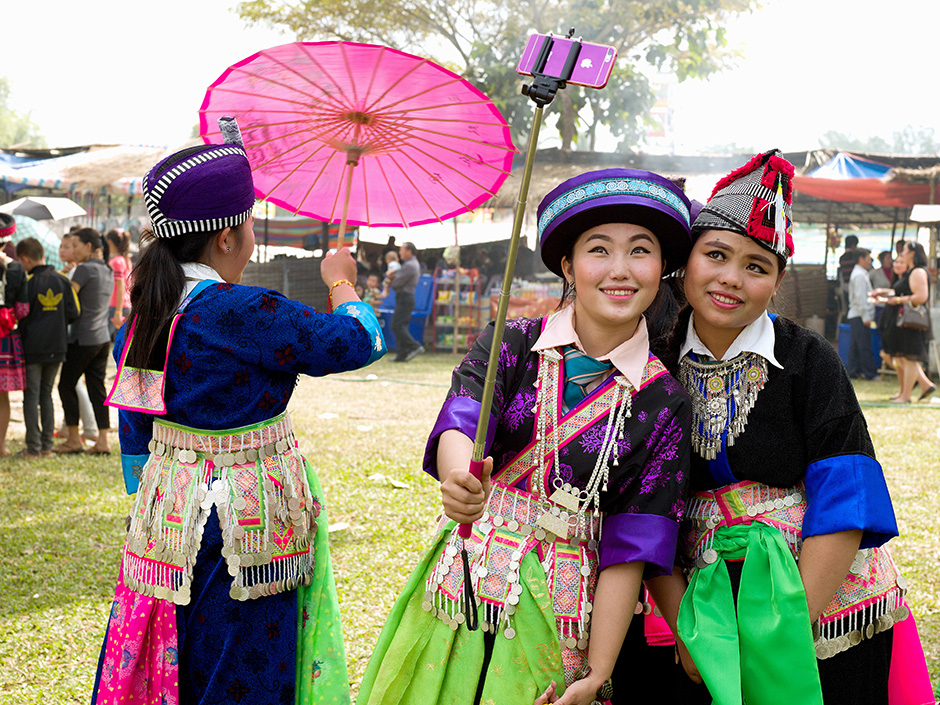 Lao PDR - Vientiane - Hmong Der (White Hmong) women wearing contemporary Hmong traditional costumes taking selfie portraits on a mobile phone at a Hmong New Year celebration